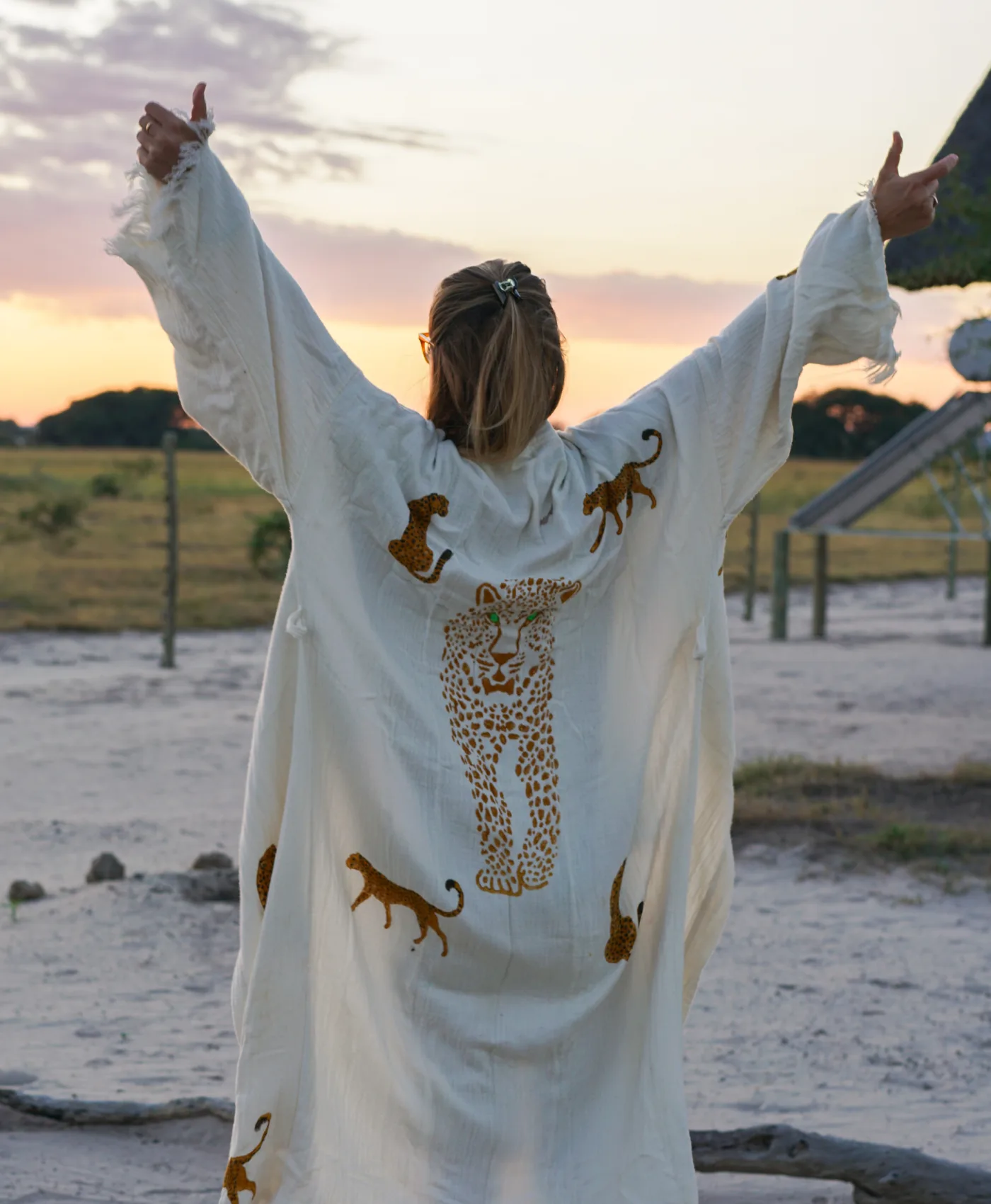 A guest in a leopard-print robe with arms raised at sunset outside the camp