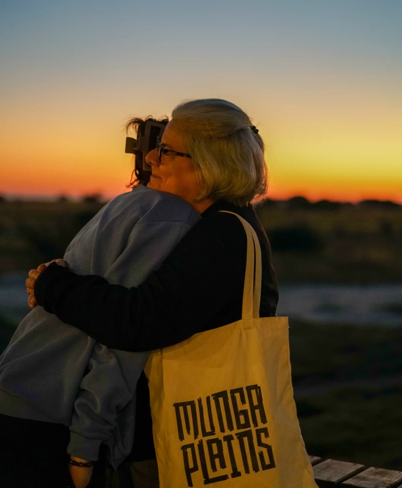 Two guests embracing as the sun sets over the floodplain