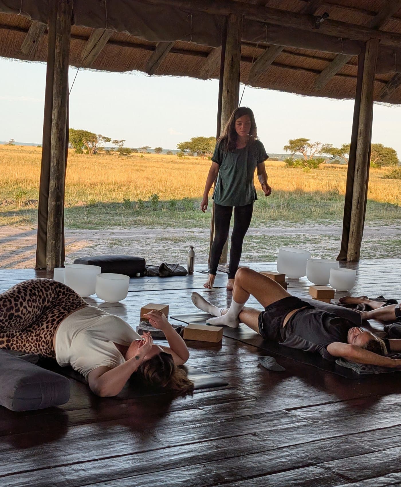 A sound bath in the yoga shala, guests lying on mats among crystal singing bowls, plains beyond