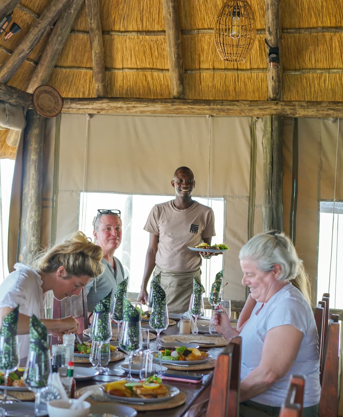 A member of the Munga Plains team serving a plate to guests at lunch under the thatched main area